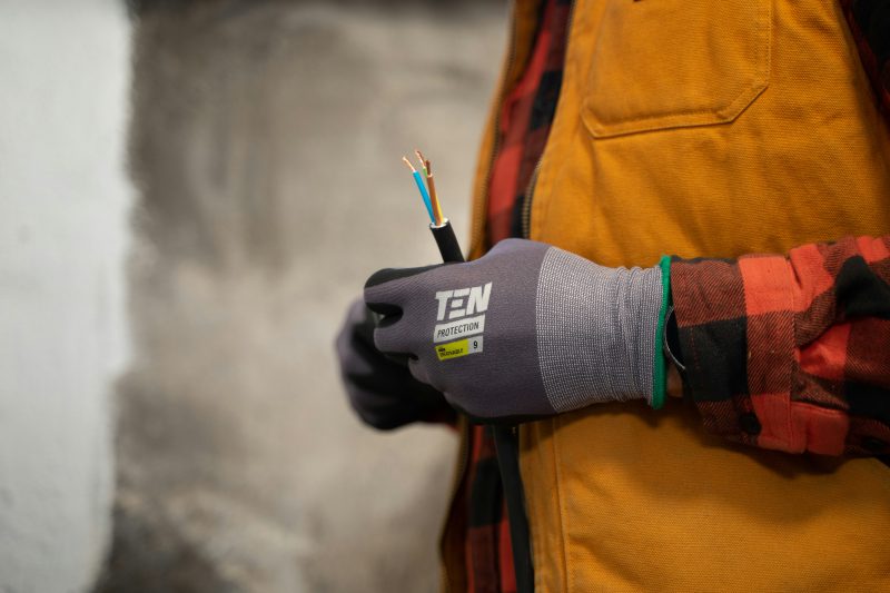 An electrician with work gloves holding a wire.