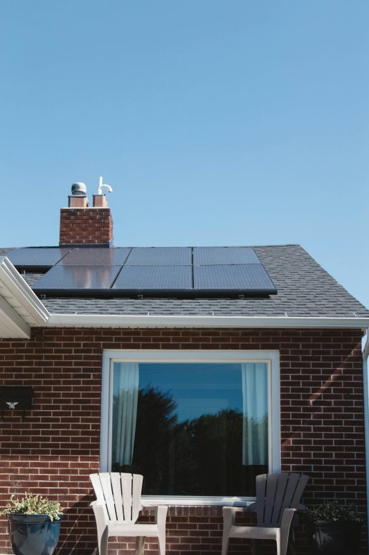 Vivint Solar - Solar Panels on roof of brick home with window and Adirondack chairs.